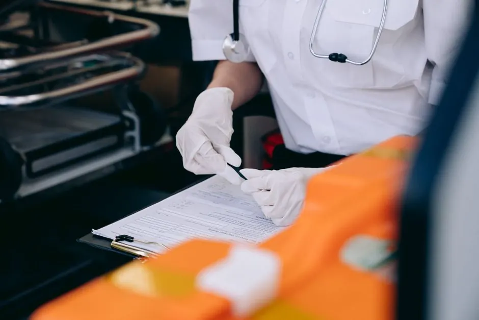 A medic wearing gloves and a stethoscope takes notes inside an ambulance.